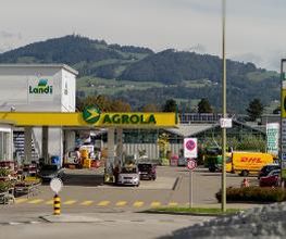 AGROLA Tankstelle in Dürnten mit Landi Laden und TopShop. Grosse Einfahrt mit Fussgängerstreifen. Rechts Totem mit Landi Logo, AGROLA Diskus und digitaler Preisanzeige