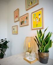 Stilvoller Eingangsbereich mit Pflanzen, Lampe und Wandbildern für eine warme Studioatmosphäre.