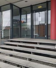 Außenansicht des Eingangbereiches mit Treppenaufstieg, Glastüre und einer roten Säule.