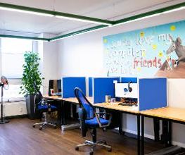 Ein Schulungsraum mit mehreren Arbeitsbereichen, die durch blaue Trennwände voneinander getrennt sind. Jeder Arbeitsplatz besteht aus 2 PC-Bildschirmen, Tastatur und Maus sowie Headset.