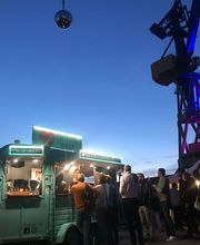 FirstLoveCoffee GmbH - Kaffee Catering Berlin - Beleuchteter Kaffeeanhänger am Abend bei Eventlocation mit Gästen, Barista-Service, Bio-Kaffee und mobilen Kaffeespezialitäten für Outdoor-Veranstaltungen.