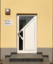 Außenansicht vom Eingang. Weiße Türe, links daneben ein WBS TRAINING Schild. Gelbe Fassade.