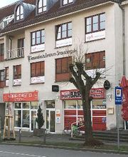 Bürogebäude hinter einer Straße. Im Erdgeschoss befindet sich eine Ladenzeile.