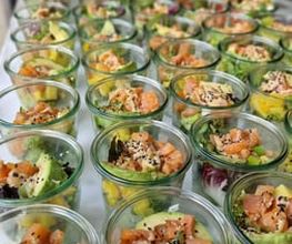 dean&david Catering | Pforzheim - Reihenweise Lachs Bowls im Glas mit Avocado, Mango, Salat, Sesam und cremigem Dressing als modernes Fingerfood für Veranstaltungen.