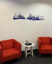Ein kleiner Sitzbereich mit zwei roten Sesseln und einem weißen Beistelltisch dazwischen. Auf dem Tisch steht eine kleine Dekoration. An der Wand ist eine blaue Silhouette von Lübeck mit dem Schriftzug „Lübeck“ angebracht.
