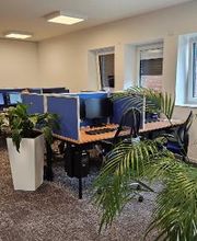 Schulungsraum mit mehreren Arbeitsplätzen mit jeweils 2 Bildschirmen, einem Bürostuhl, Tastatur und Maus. Im Raum mehrere Topfpflanzen