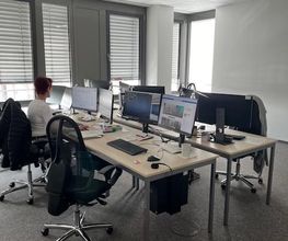 Ein Schulungsraum mit mehreren Arbeitsbereichen. Jeder Arbeitsplatz besteht aus 2 PC-Bildschirmen, Tastatur und Maus sowie Headset.