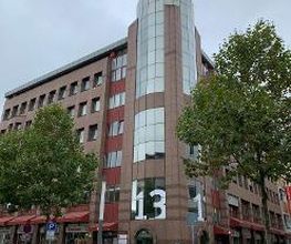 Außenansicht vom Gebäude an einer Straße. Hellbraune Fassade mit vielen Fenstern.