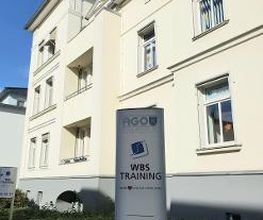 Beschilderung WBS TRAINING vor gelbem Haus.