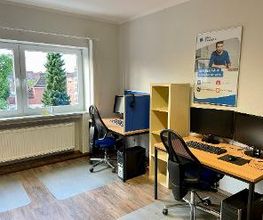 Ein Schulungsraum mit zwei Arbeitsplätzen. Jeweils mit 2 Bildschirmen, einem Bürostuhl, Tastatur, Maus und Headset. Dazwischen ein Regal und ein Poster der WBS TRAINING an der Wand. Der Boden ist mit Rollenschutz versehen. 