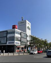 Gebäude an einer Straße mit parkenden Autos und Bäumen. Auf dem Gebäude ein Schild von Penny.