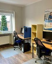 Ein Schulungsraum mit zwei Arbeitsplätzen. Jeweils mit 2 Bildschirmen, einem Bürostuhl, Tastatur, Maus und Headset. Dazwischen ein Regal und ein Poster der WBS TRAINING an der Wand. Der Boden ist mit Rollenschutz versehen. 