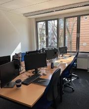 Schulungsraum mit einer großen Fensterfront und Schreibtischen die mit Bildschirmen, Tastaturen, Mäusen und Headsets ausgestattet sind. 