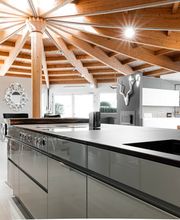 Diese exklusive Designküche verbindet moderne Eleganz mit natürlicher Architektur. Im Vordergrund stehen eine großzügige Kochinsel mit integriertem Bora Kochfeld, eine mattschwarze Quooker Design-Armatur und ein flächenbündiges Spülbecken. Die offene Raumgestaltung mit beeindruckender Holzbalkendecke, hochwertigen Materialien und klaren Linien schafft ein stilvolles Wohnambiente. Die hochwertige LEICHT Küche fügt sich harmonisch in den lichtdurchfluteten Wohnraum ein und vereint Funktionalität mit zeitlosem Küchendesign.