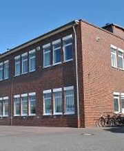 Backsteingebäude vor dem Autos und Fahrräder geparkt sind.