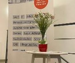 Roll Up WBS Training. Davor steht ein kleiner weißer Tisch mit einem Blumenstrauß.