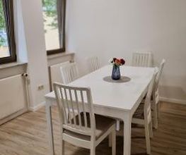 Weißer Tisch mit 6 Stühlen im Pausenraum. Auf dem Tisch steht eine Vase mit Blumen.