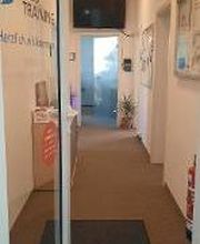 Eingangstür und Zugang zur Verwaltung. Am Ende des kurzen Flurs ein Bildschirm, links ein Regal.