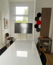 Besprechungsraum mit Tisch, Stühlen und Bildschirm. 