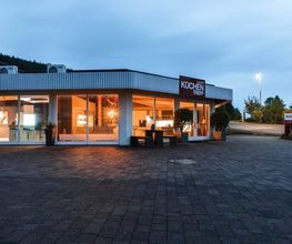 Die Außenansicht zeigt das Küchenstudio Küchentreff Liebold in den Abendstunden. Große Glasfronten geben den Blick auf die stilvoll beleuchtete Küchenausstellung frei und präsentieren moderne Designküchen in hochwertigem Ambiente. Die einladende Architektur, das markante Küchentreff-Logo und die helle Innenbeleuchtung vermitteln Kompetenz, Qualität und Inspiration für individuelle Küchenplanung.