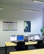 Seminarraum mit 3 Arbeitsplätzen jeweils mit 2 Bildschirmen, einem Bürostuhl, Tastatur, Maus und Headset. An der Wand Plakate und ein Wandkalender.