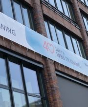 Eine Hausfassade an der ein Banner mit der Aufschrift „40 Jahre WBS TRAINING“ angebracht ist.
