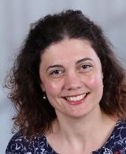 Frau mit schulterlangen dunklen Haaren und gemusterter Bluse.
