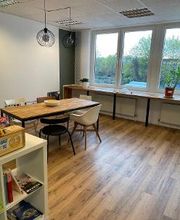 Ein großer Holztisch mit Stühlen im Aufenthaltsraum. Ein weißes Bücherregal und Fensterfront mit Blick ins Grüne.