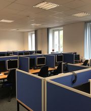 Ein Schulungsraum mit mehreren Arbeitsbereichen, die durch blaue Trennwände voneinander getrennt sind. Jeder Arbeitsplatz besteht aus 2 PC-Bildschirmen, Tastatur und Maus sowie Headset.