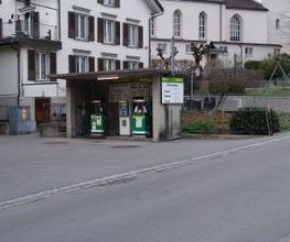 AGROLA Tankstelle in Ebnat-Kappel. Zwei Tanksäulen unter kleinem Unterstand. Im Hintergrund mehrere Gebäude und Spielplatz.
