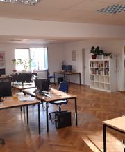 Ein offener Lernbereich mit mehreren PC-Arbeitsplätzen und Regalen. Jeder Arbeitsplatz verfügt über 2 Bildschirmen, einer Tastatur und Maus sowie einem blauen Bürostuhl.