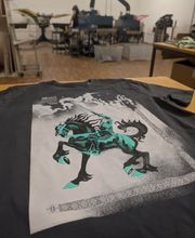 Brillanter Mehrfarbdruck mit feinen Rasterverläufen und Sonderfarben (Türkis/Schwarz/Weiß) auf dunklem Baumwollshirt. Wir realisieren auch hochkomplexe Artworks im Siebdruckverfahren mit Farbmischung nach PANTONE. Höchste handwerkliche Präzision für anspruchsvolle Kollektionen von Modelabels, Bands und Künstlern aus Leipzig.