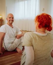 Persönliche Unterrichtssituation mit Lehrer und Teilnehmerin auf Yogamatten im warmen Studioambiente. Das Bild wirkt nahbar, freundlich und einladend.