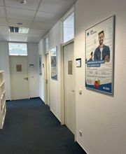 Flur mit Plakaten an der Wand und weißen Türen zu Räumlichkeiten.