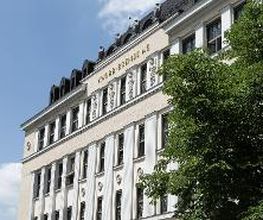 Front of the historic Knorr-Bremse Group building at the company's headquarters in Munich, with the words Knorr-Bremse AG in gold letters at the top. To the right of the building is a large chestnut tree with green leaves.