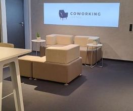Aufenthaltsbereich mit Sofas und Tischen. Über einen Beamer wird ein Bild an die Wand geworfen, auf dem "Coworking" steht.