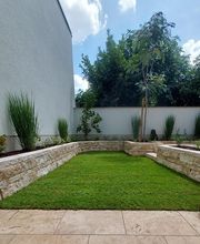 Naturstein-Terrasse mit angrenzendem Garten, junger Baum, Ziergräsern und Rollrasen – stilvolle, moderne Gartengestaltung.