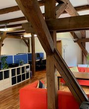 Trainingsraum mit Fachablagen und Schreibtischen und angrenzenden Sofabereich mit Tisch.