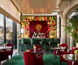 Vibrant cocktail bar at The Woodward Geneva with red velvet chairs, colorful glass accents, and lake views.