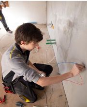 Unser Montage-Elektriker Lehrling der dabei ist ein Kabel durch die Wand bei einem Gebäude zu verlegen. Die Arbeiten reichen von der Roh- bis zur Endmontage.