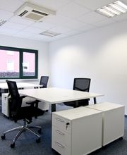 Büroraum mit 4 Arbeitsplätzen. 2 weiße Tische, 4 schwarze Bürostühle, 4 weiße Rollcontainer, Fenster.