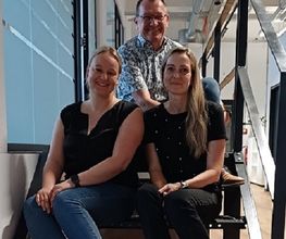 Team aus 3 Personen welche auf einer Treppe sitzen und freundlich lächeln.