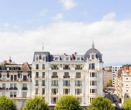 Exterior facade of The Woodward Geneva, a grand lakeside hotel with classic architecture and tree-lined streets.