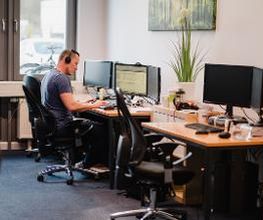 Ein Mann mit Headset sitzt an einem PC-Arbeitsplatz.