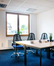 Pausenraum mit großem Tisch und mehreren Arbeitsplätzen und Bürostühlen. In der Ecke eine Stehlampe, an der Wand ein Sticker mit Aufschrift: Mach einfach mal Pause.