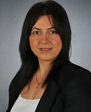 Eine Frau mit schwarzen Haaren, schwarzem Blazer und weißem Oberteil.