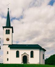 Die heutige Kirche wurde am 10. August 1852 eingeweiht. Sie steht auf dem Hügel, auf dem die erste Kapelle in Freirachdorf im 15. Jahrhundert gebaut wurde und wegen Baufälligkeit abgerissen werden musste. Besondere Schmückstücke sind die Sakramentsfenster im Chorraum, auf denen Christus in der Mitte, Mose und Paulus zu je einer Seite abgebildet sind. Der große Kronleuchter im Kirchenschiff ist aus 400 Jahre altem Eichenholz geschnitzt.