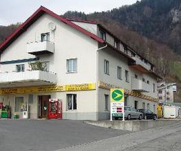 AGROLA Tankstelle in Weesen bei FLY Garage. Eine Tanksäule direkt unter Balkon gelegen. Daneben Zahlterminal und Selecta Automat. Im Vordergrund Strasse mit Einfahrt.