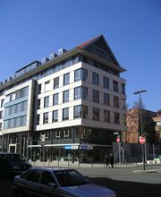 Ein vierstöckiges weißes Gebäude mit Spitzdach an einer Straßenkreuzung.