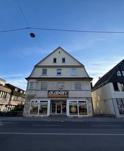 Academy Fahrschule Baumann - Stuttgart Vaihingen - Breite Straßenansicht einer Fahrschule in Stuttgart-Vaihingen mit auffälliger Beschilderung, Schaufenstern und gut erreichbarer Lage an einer Hauptstraße.